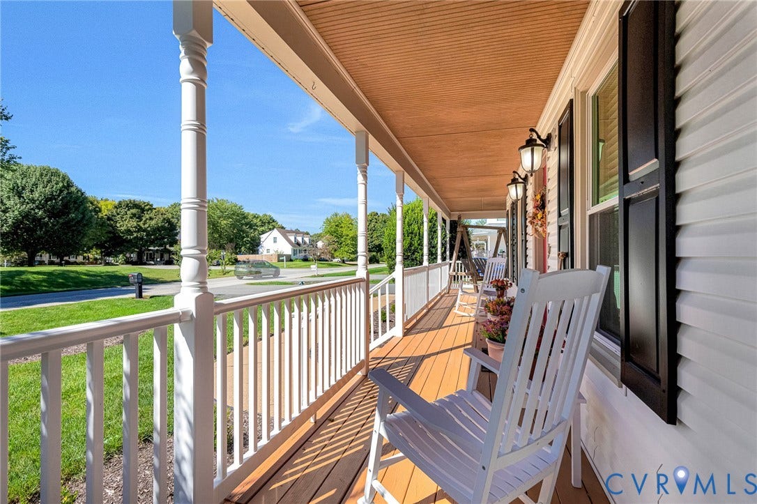 Expansive covered front porch with a wood-finish floor, white baluster railing, white columns, and exterior wall sconces