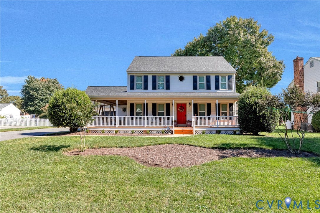 Two-story exterior with a covered front porch, white railing, red entry door, and dark shutters
