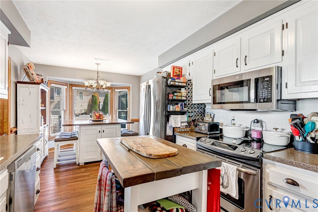 Kitchen featuring white cabinetry, stainless steel appliances, wood-finish flooring, and a bay window