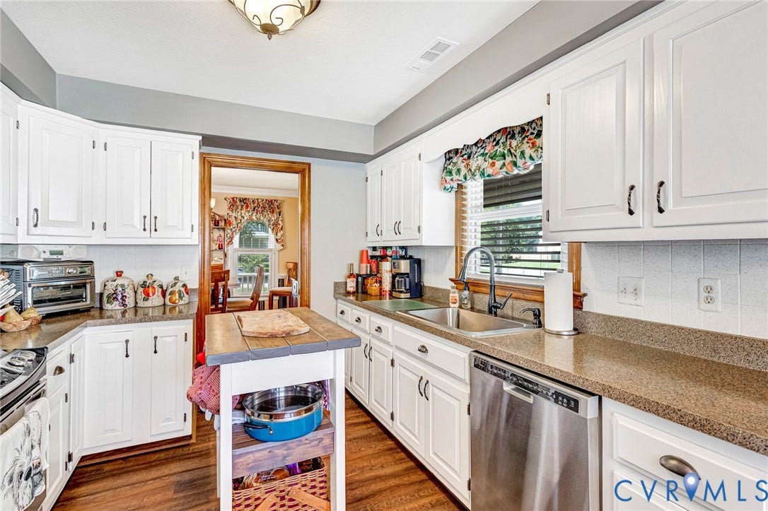 White cabinetry, wood-finish flooring, stainless steel dishwasher, and a double basin sink with a black faucet