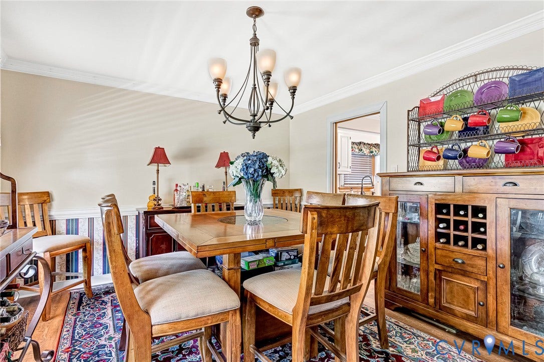 Dining area featuring wood-finish flooring, a decorative chandelier, crown molding, and a built-in wood cabinet with glass-front doors and wine storage