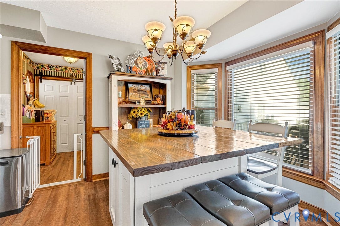 Wood-finish flooring, built-in shelving, bay windows with blinds, and a central island with a wood-finish countertop