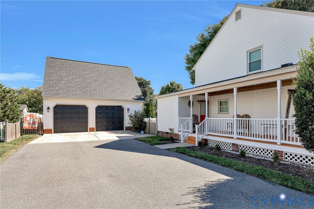 Two-car detached garage with a shingled roof, asphalt driveway, and a covered front porch featuring white railings