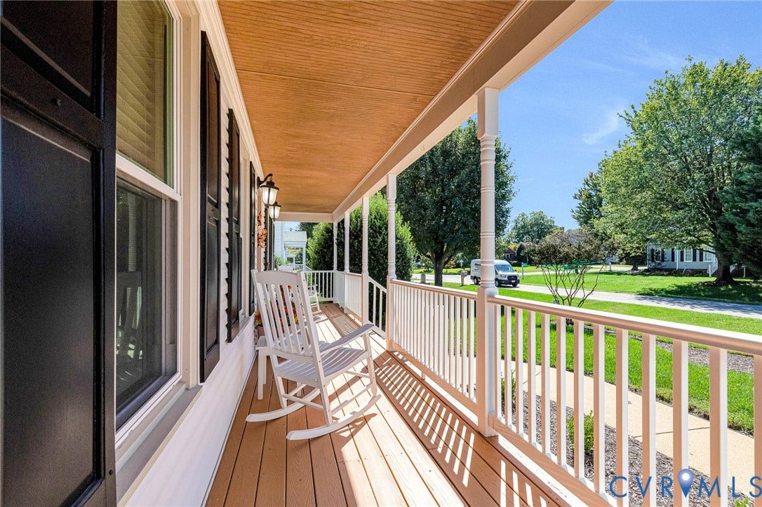 Expansive front porch featuring wood-finish decking, decorative white railings, and exterior wall sconces
