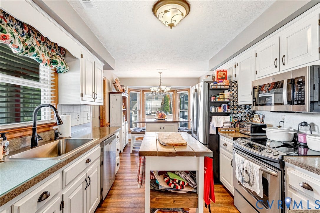 Kitchen featuring white cabinetry, stainless steel appliances, wood-finish flooring, and a dining area with a bay window