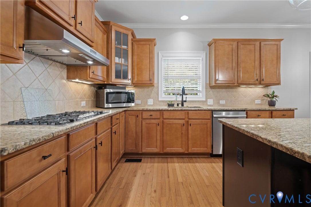 Warm wood cabinetry with glass-front upper storage and brushed nickel hardware anchors this kitchen, featuring granite countertops, stainless steel appliances including a gas cooktop and built-in microwave, diagonal tile backsplash, and an oversized island with additional counter space