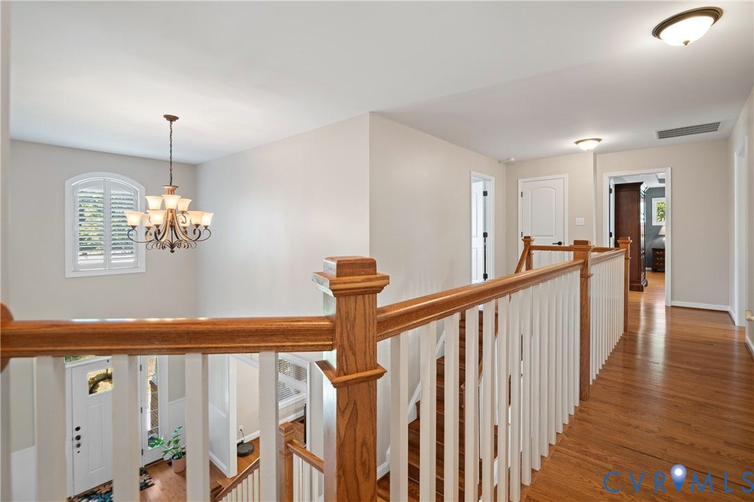 Hardwood flooring, wood banister with white spindles, arched window with plantation shutters, overhead chandelier, and recessed lighting