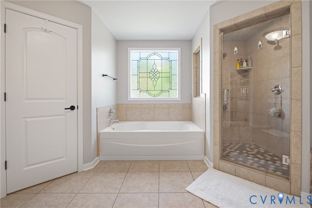 Built-in soaking tub with tiled surround, glass-enclosed shower with a patterned tile floor, decorative privacy window, and large format floor tiling