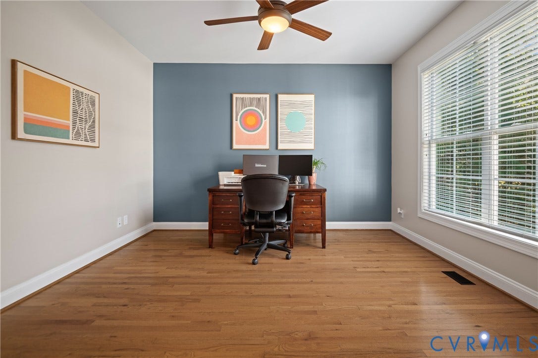 Wood-finish flooring, accent wall, ceiling fan with integrated lighting, and a large window with blinds