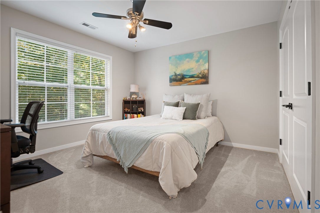 Light gray wall paint, light gray carpet, window with horizontal blinds, built-in ceiling fan with light, and white paneled door with black hardware