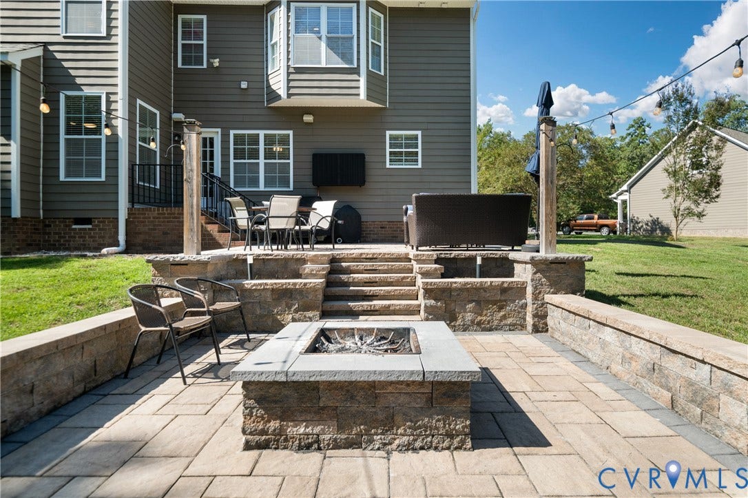 Multi-tiered paver patio with a built-in stone fire pit, stone retaining walls, and outdoor string lighting