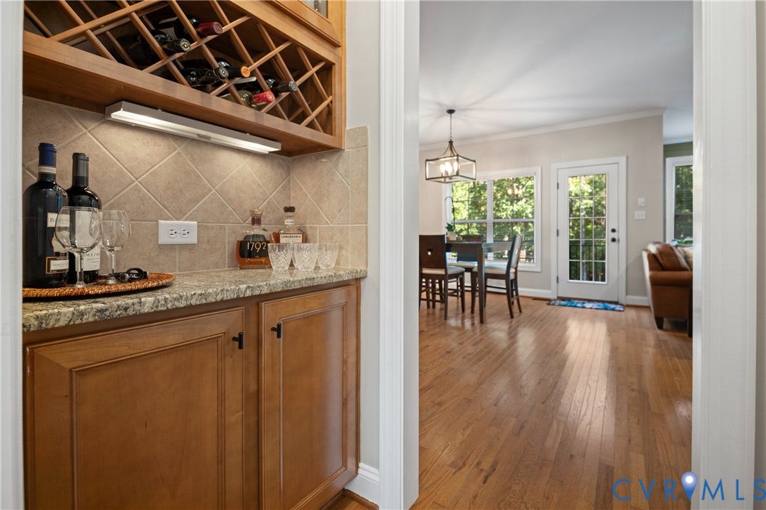 Built-in wine rack, tile backsplash, under-cabinet lighting, wood-finish flooring, and a glass-paned exterior door