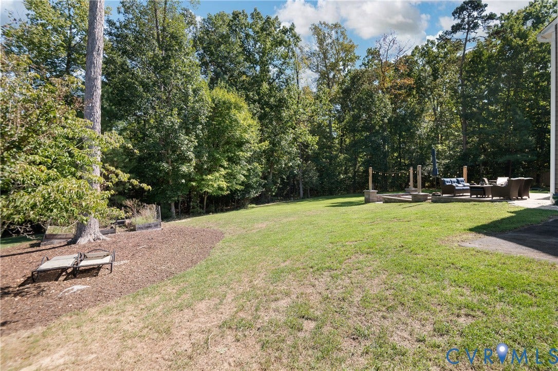 Expansive grassy lawn with a dedicated patio area featuring a built-in fire pit, surrounded by mature trees