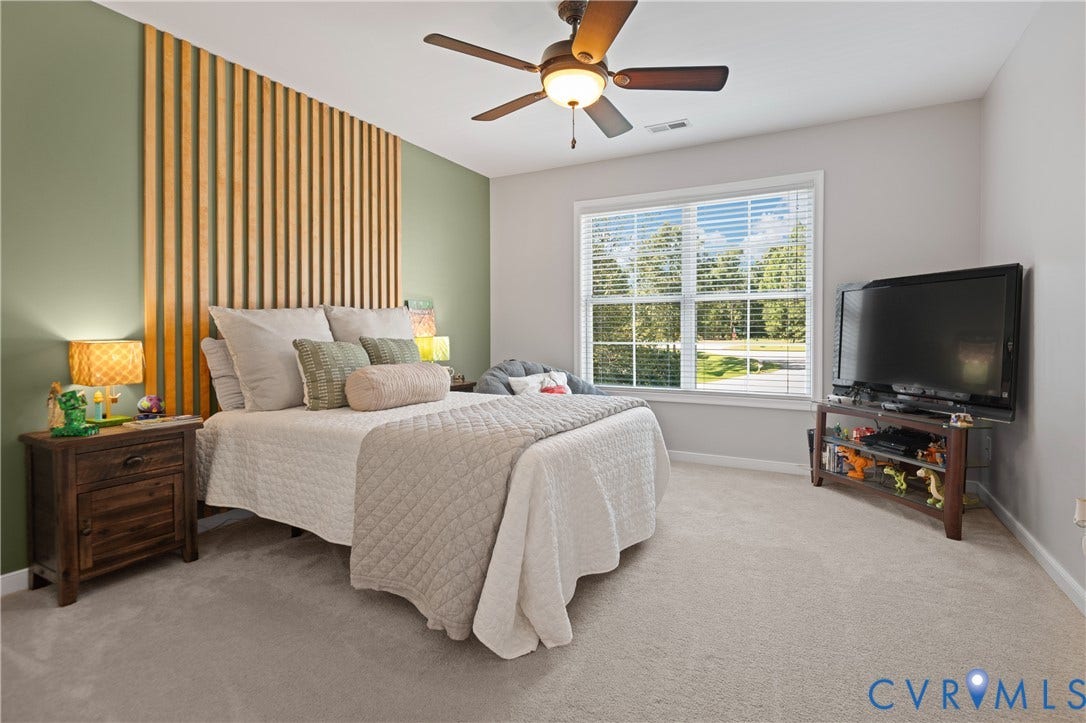 Plank accent wall, ceiling fan with integrated lighting, window with blinds, light-toned carpet flooring, and painted walls