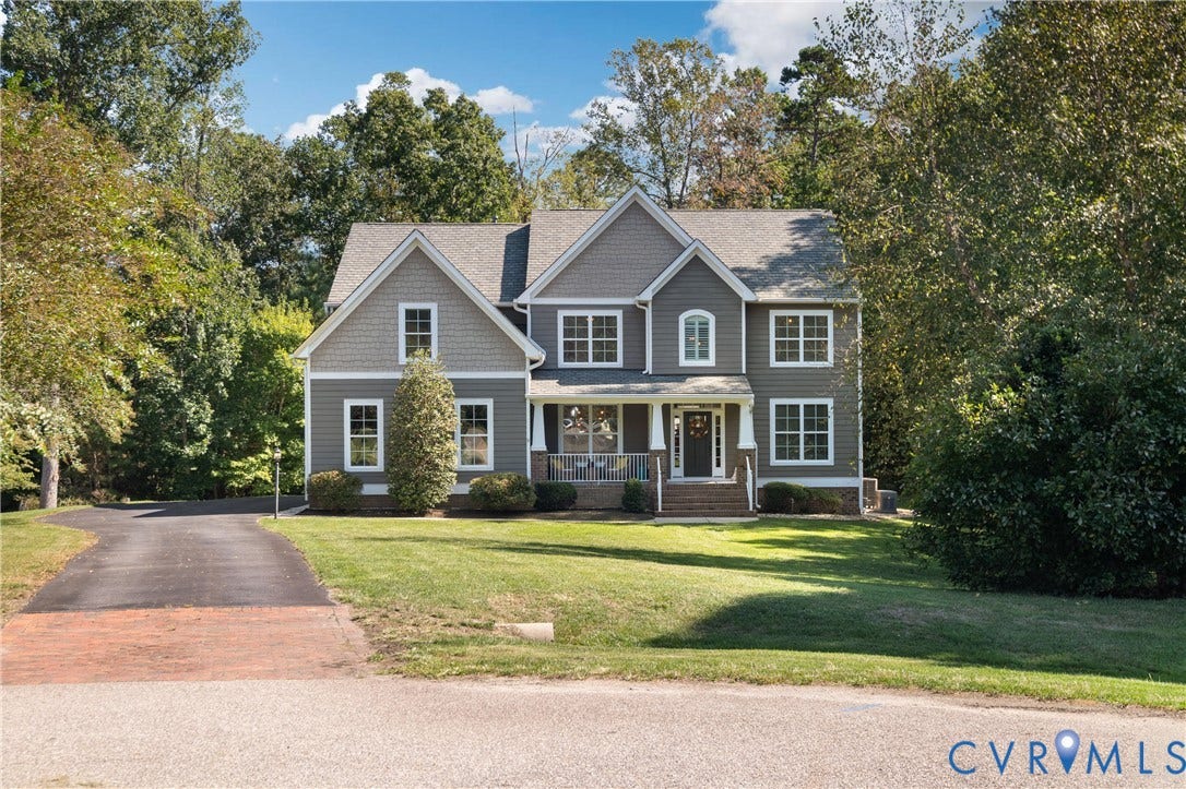 Two-story residence with a gray siding exterior and white trim, featuring a covered front porch with white pillars, a gabled roofline, and multiple windows