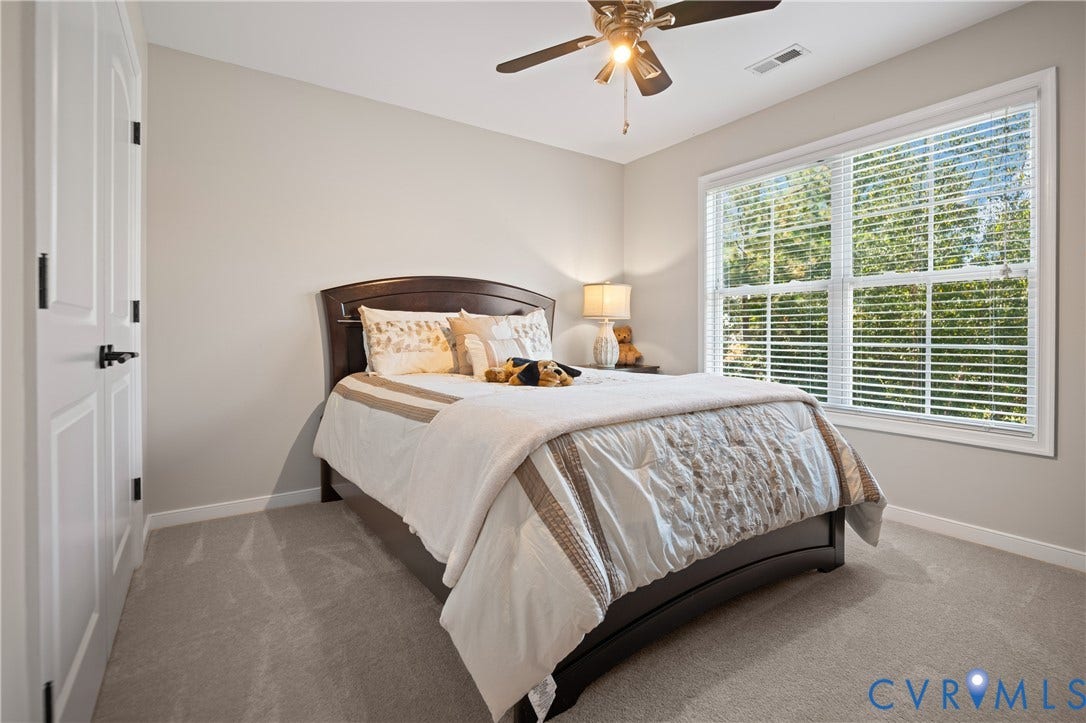 Neutral wall paint, light gray carpeting, ceiling fan with integrated lighting, a large window, and white interior doors with black hardware