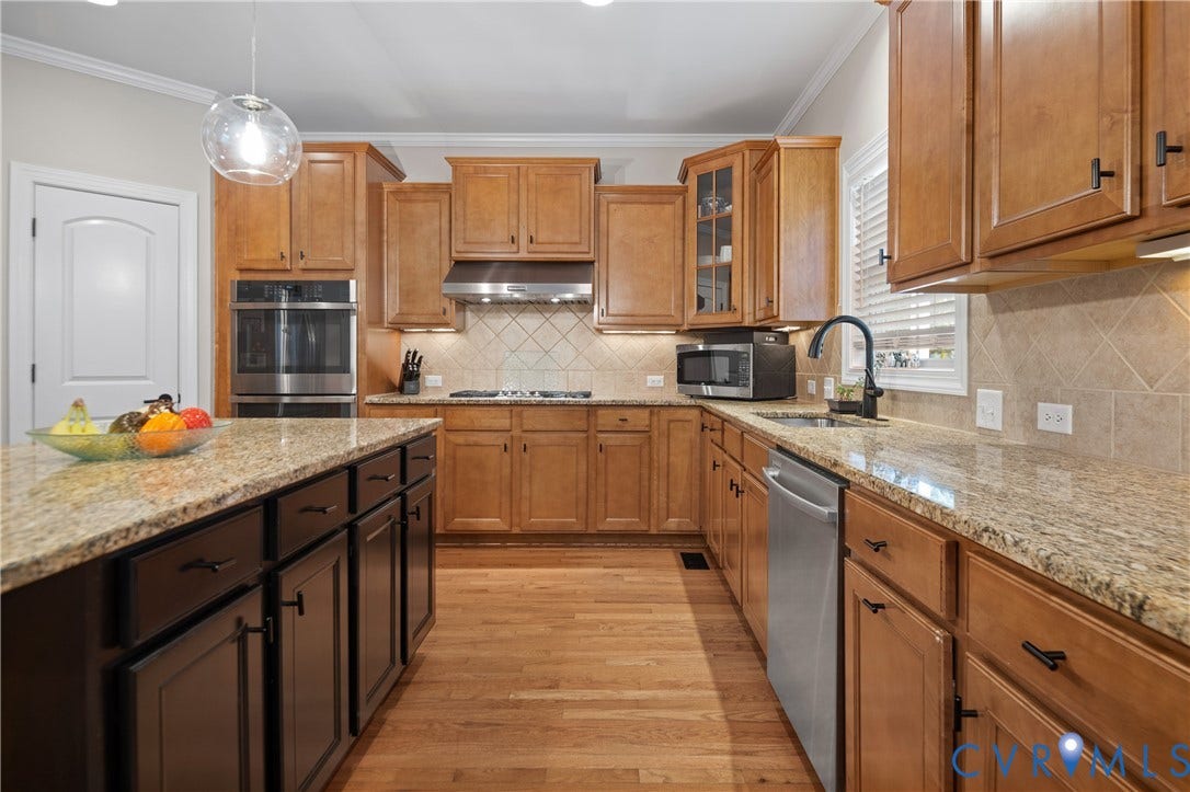 Spacious kitchen featuring natural wood cabinetry, light-toned countertops, a multi-tone island, and stainless steel appliances