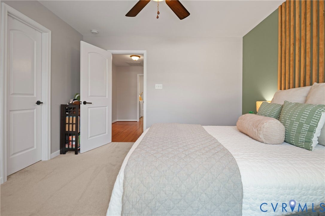 Carpet flooring, an overhead ceiling fan, white paneled doors with black hardware, and an accent wall featuring vertical wood slat detailing