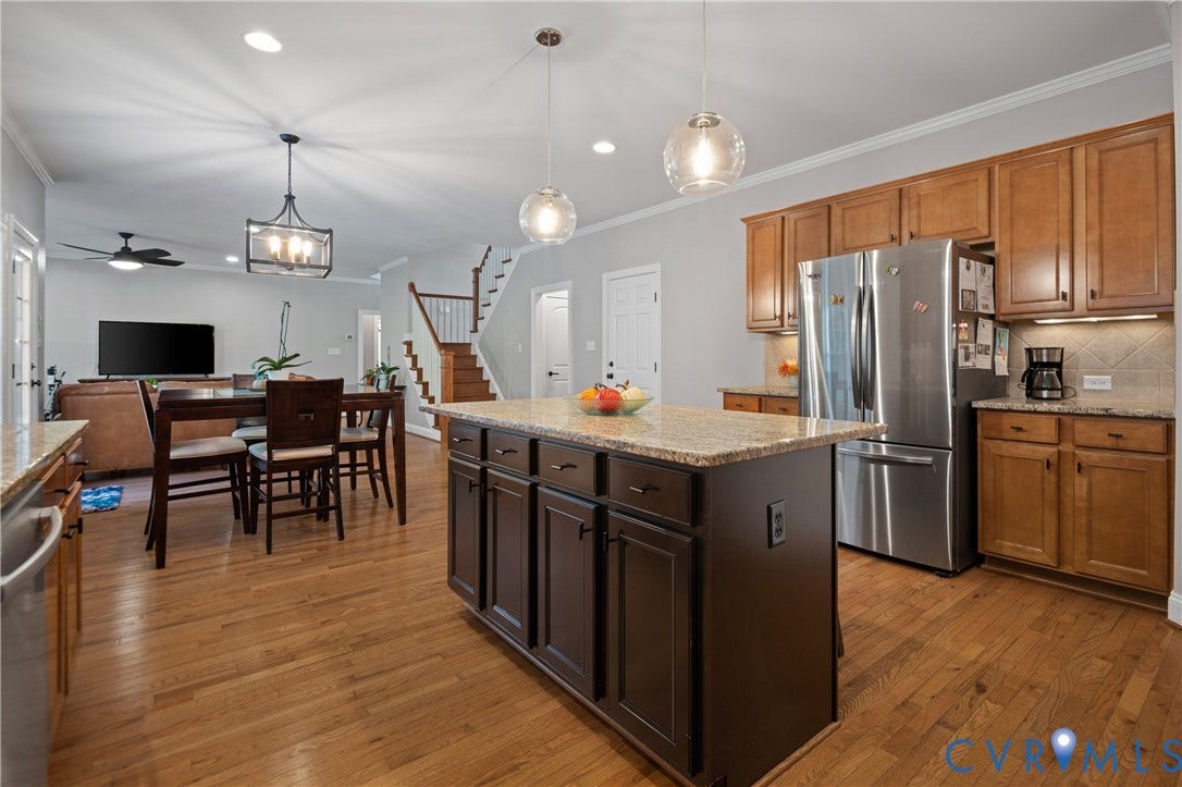 Wood-finish flooring throughout, kitchen island with granite countertop, stainless steel refrigerator, wood cabinetry, and recessed lighting