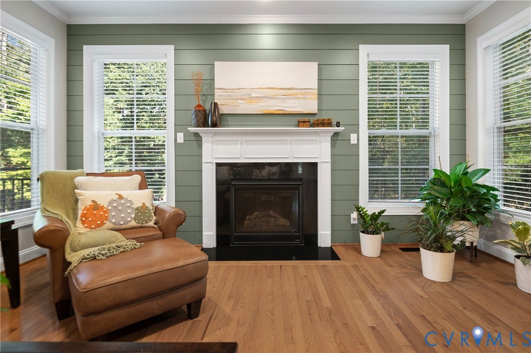 Spacious room featuring wood-finish flooring, a fireplace with a white mantel and dark hearth, a shiplap accent wall, and multiple large windows