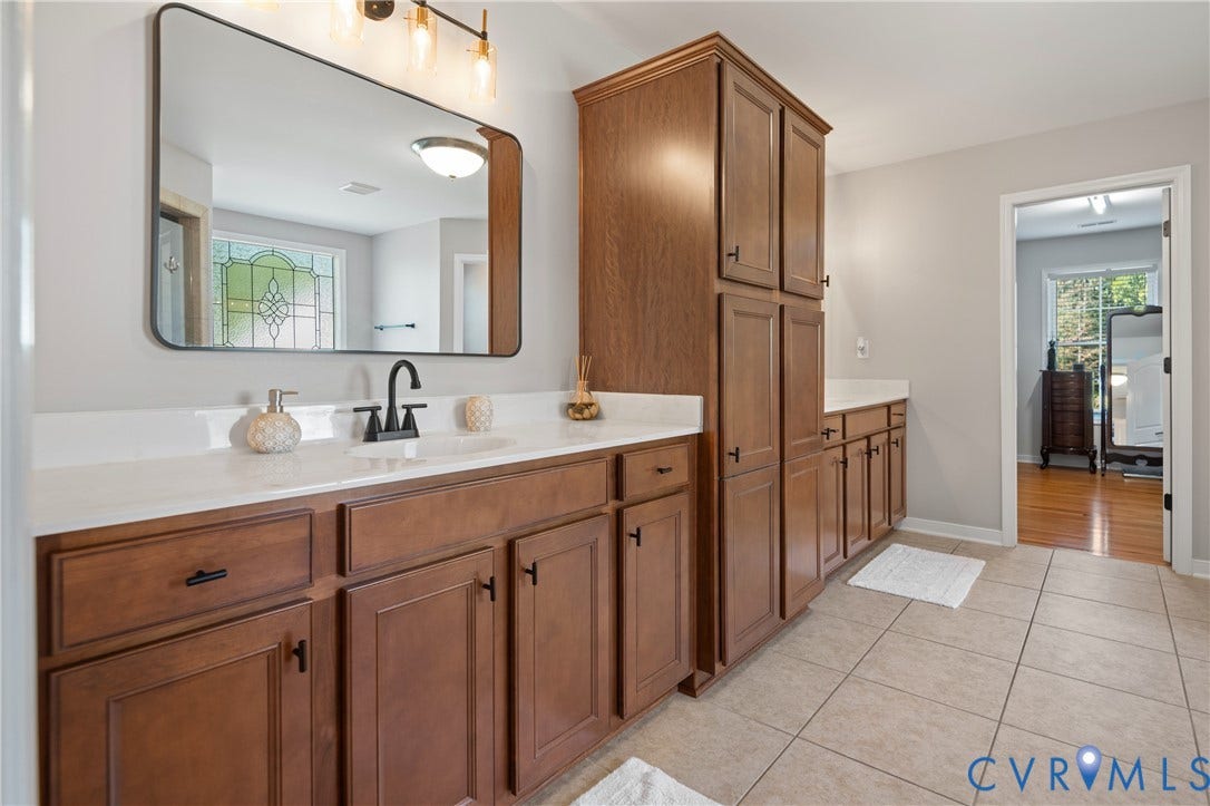 Dual vanity with a white countertop, multiple wood-finish cabinetry, and a large wall-mounted mirror