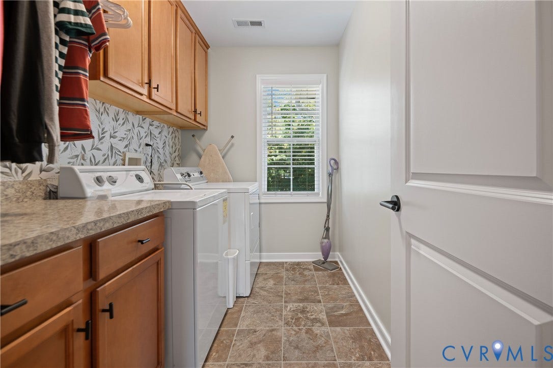 Wood-finish cabinetry, patterned backsplash, durable countertop, and window with blinds