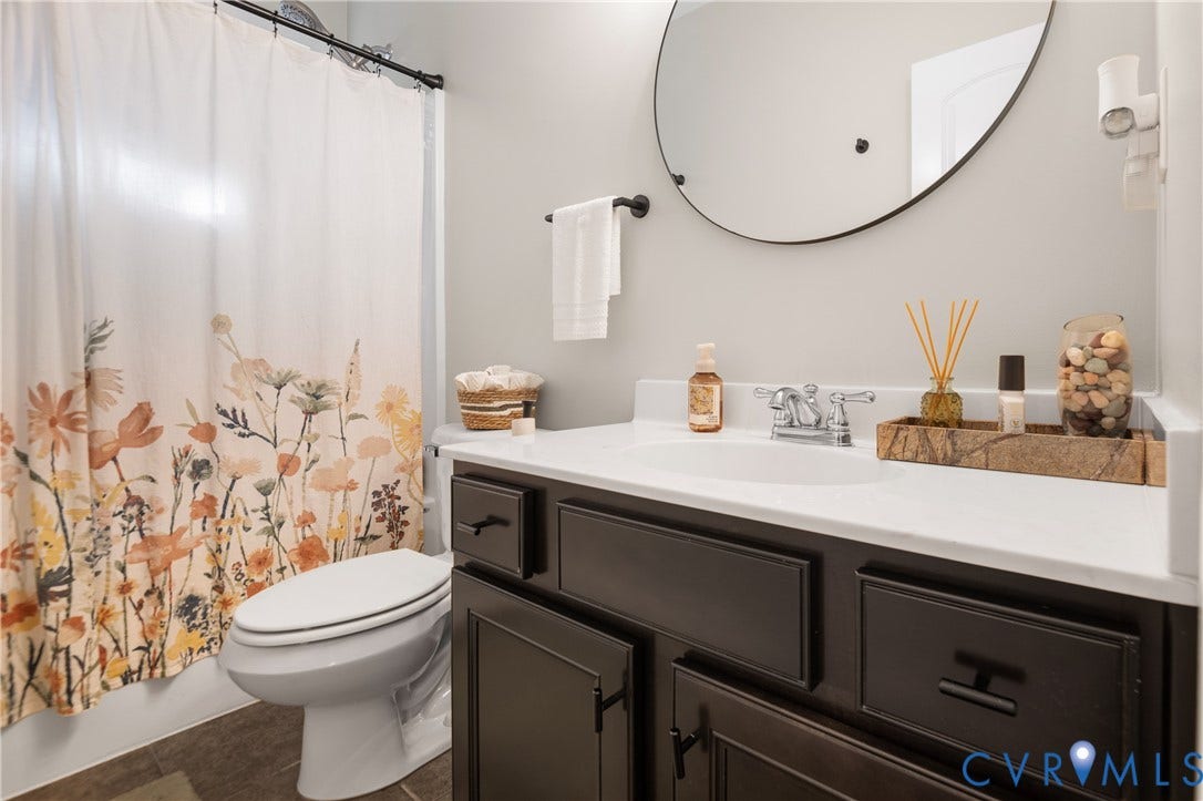 Vanity with a white countertop and dark wood-finish cabinetry, a circular mirror, and a wall-mounted towel bar