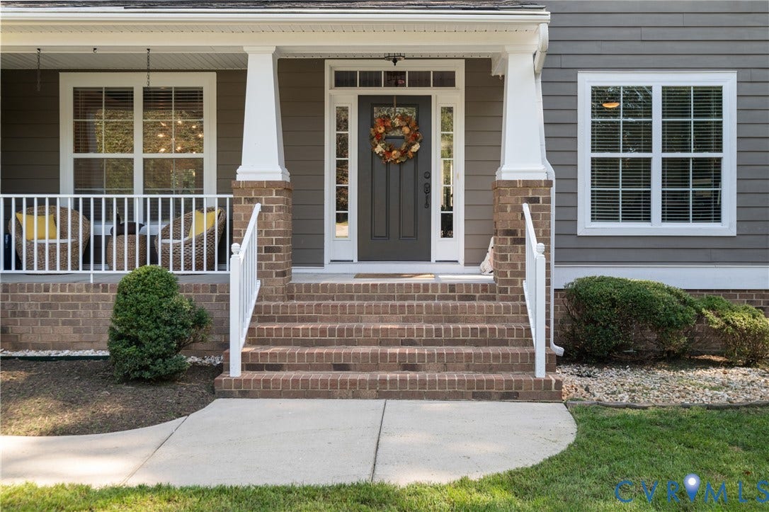 Brick front steps and foundation with white porch railings, gray siding, and a dark entry door