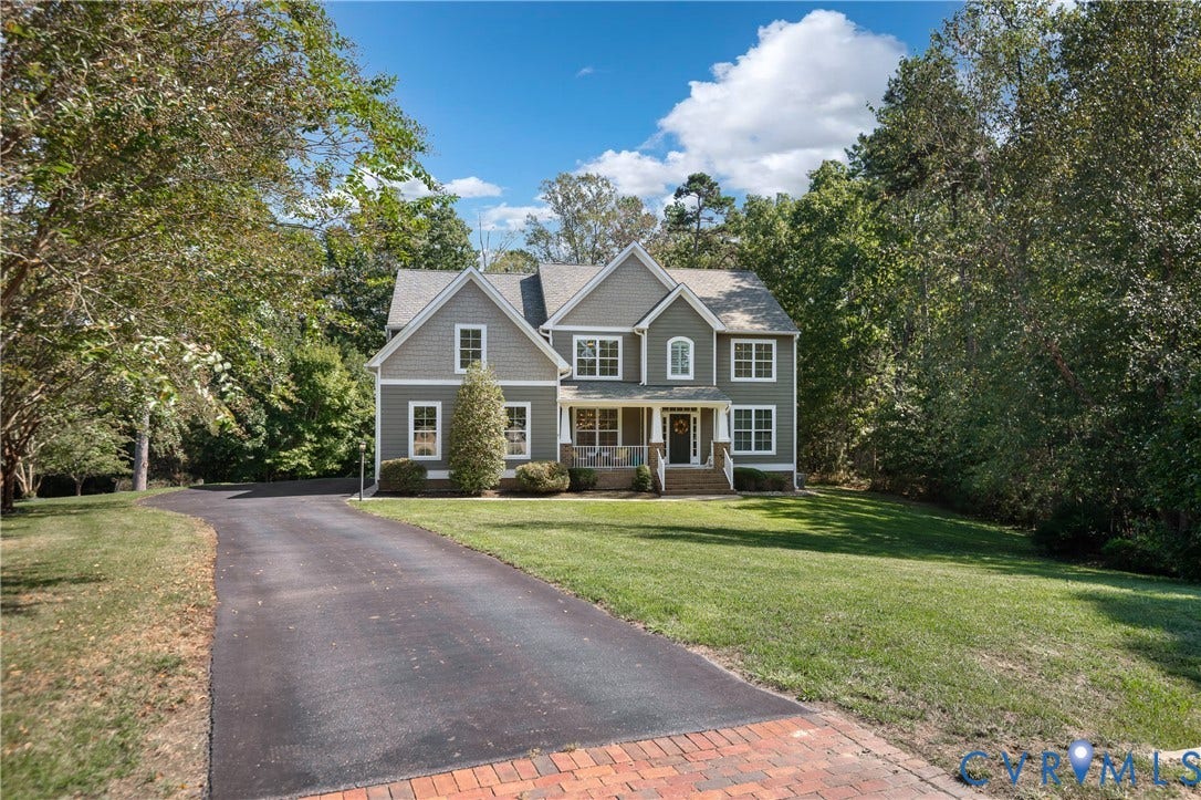 Gray siding exterior with white trim, a covered front porch, an asphalt driveway, a brick driveway accent, and a landscaped lawn