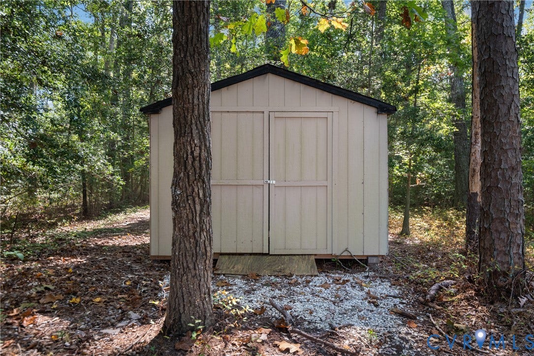 Detached storage shed with dual-paneled doors, wood siding, and a sloped roof set on a gravel foundation