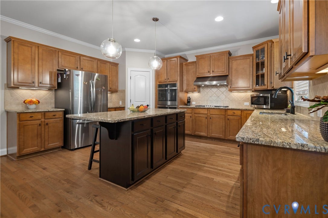 Kitchen featuring wood-finish flooring, granite countertops, wood cabinetry, a center island with seating, and stainless steel appliances