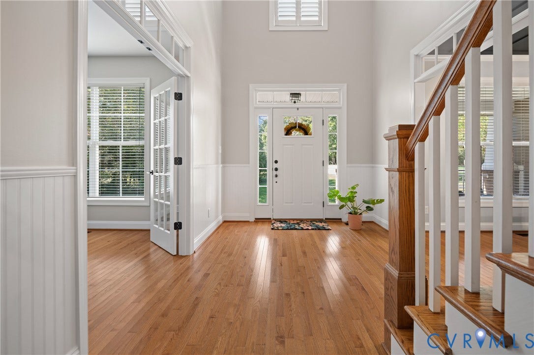 Foyer featuring wood-finish flooring, wainscoting, a prominent staircase with wood railing, French doors, and a transom window above the main entry