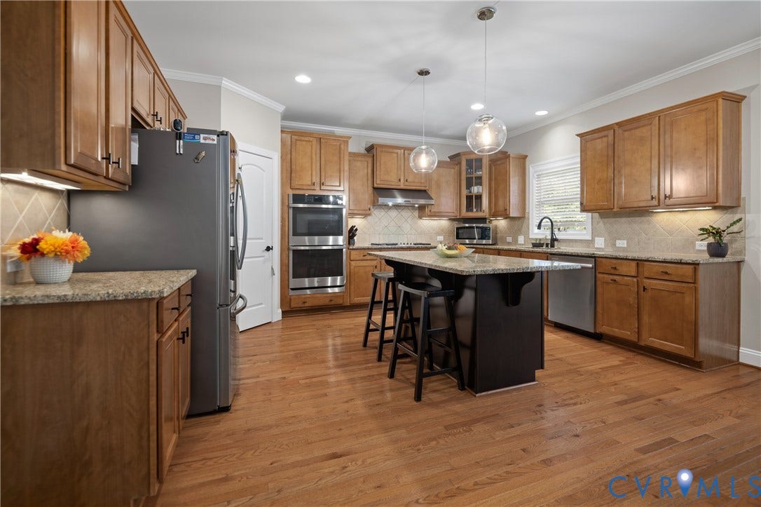 Hardwood flooring, wood cabinetry, built-in double ovens, center island with stone countertop, and pendant lighting