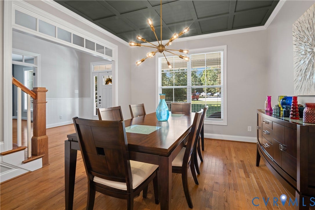 Hardwood flooring, painted coffered ceiling, modern chandelier, window with blinds, and white wainscoting