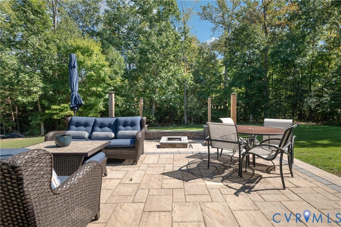 Expansive paver patio featuring a built-in fire pit, surrounded by mature trees and manicured lawn