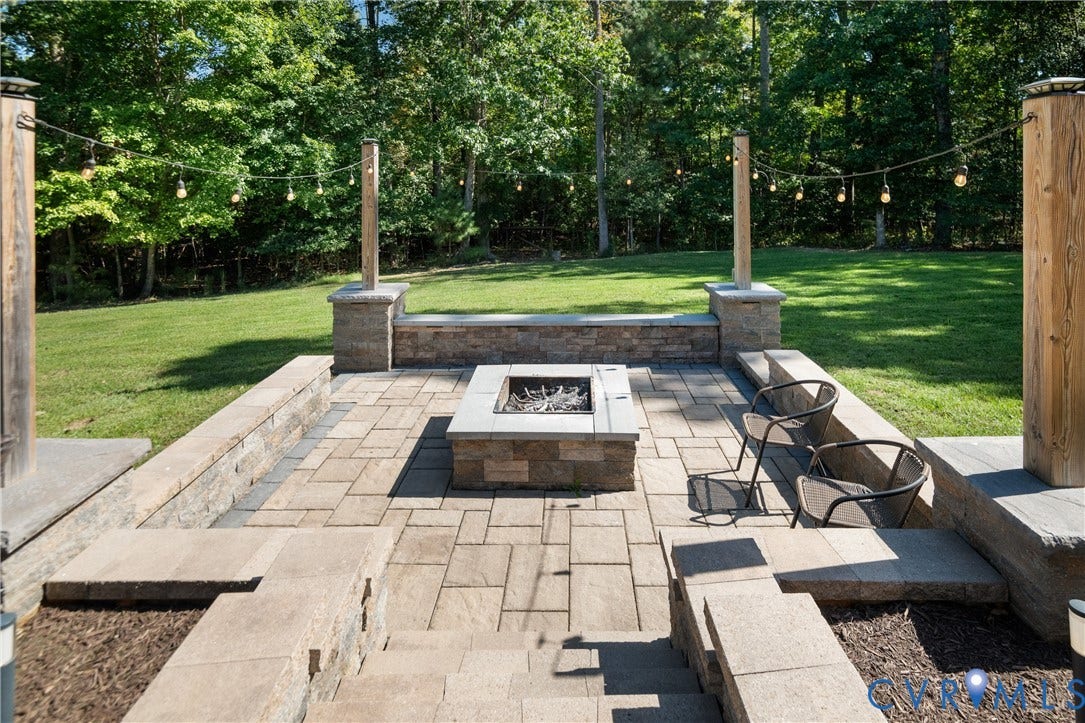 Expansive paver patio featuring a stone fire pit, built-in stone seating, and integrated stone landscaping walls