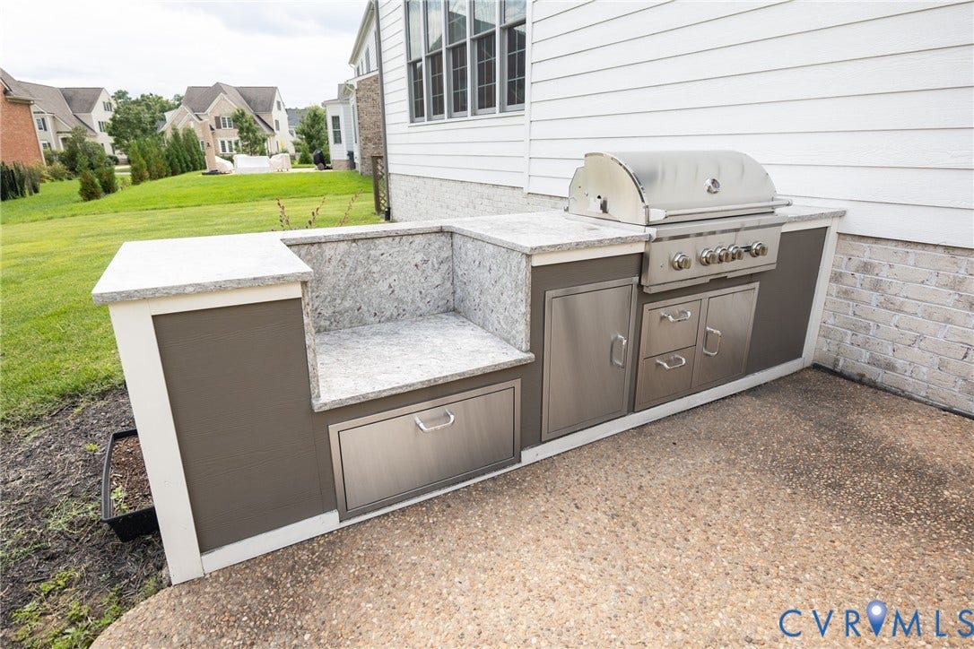 Built-in outdoor kitchen with integrated grill, stainless steel cabinetry, granite countertops and a space for a smoker or outdoor pizza oven.