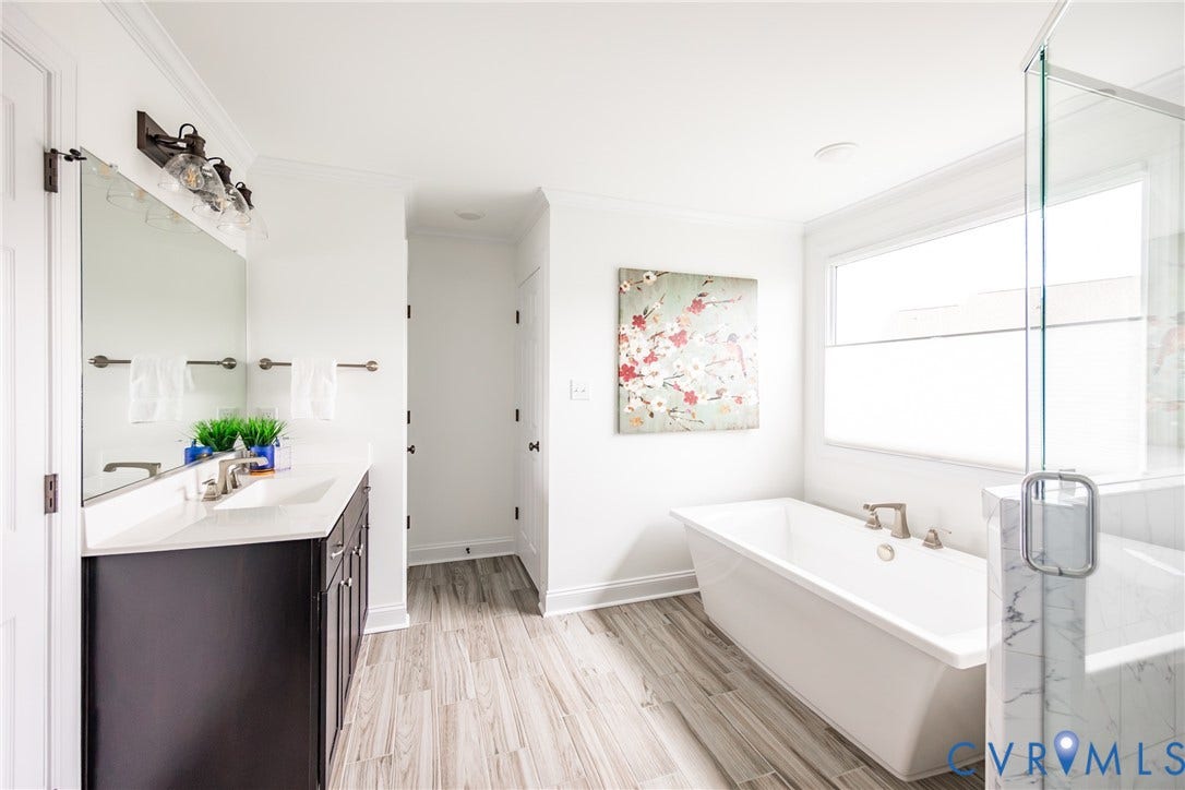 Alternate primary bathroom view that shows the second vanity sink as well at the linen closet to the back left and the water closet to the back right. The window coverings by the soaking tub are top-down bottom-up style to allow ample light to shine in while also ensuring privacy.