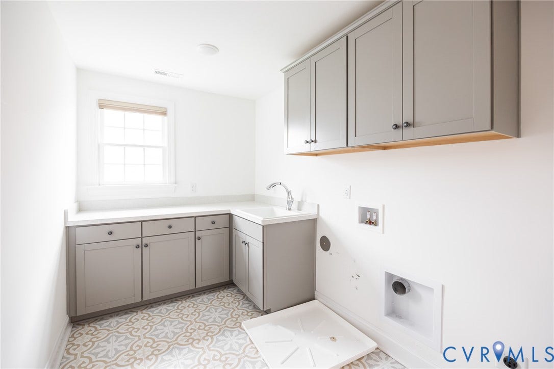 Just outside of the primary suite is a large dedicated laundry room featuring cabinetry with ample storage, a utility sink with a stainless steel faucet, washer and dryer hookups, tile flooring, and abundant natural light from a multi-pane window.