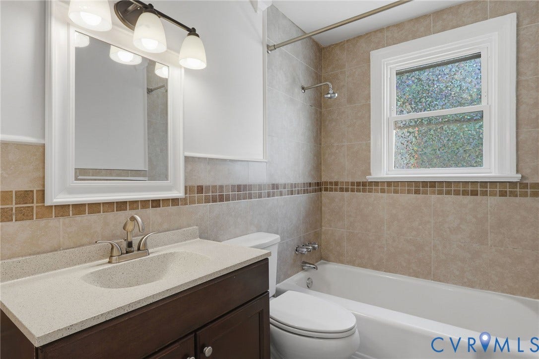 5108 Forest Hill Avenue, Westover Hills Area, Richmond, VA 23225 First floor full bathroom. Vanity with integrated sink and chrome faucet, framed mirror, three-light vanity fixture, tiled shower with bathtub, and a window.
