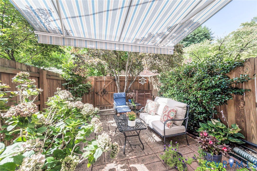 Paved patio featuring a striped retractable awning, privacy fencing, and established plantings