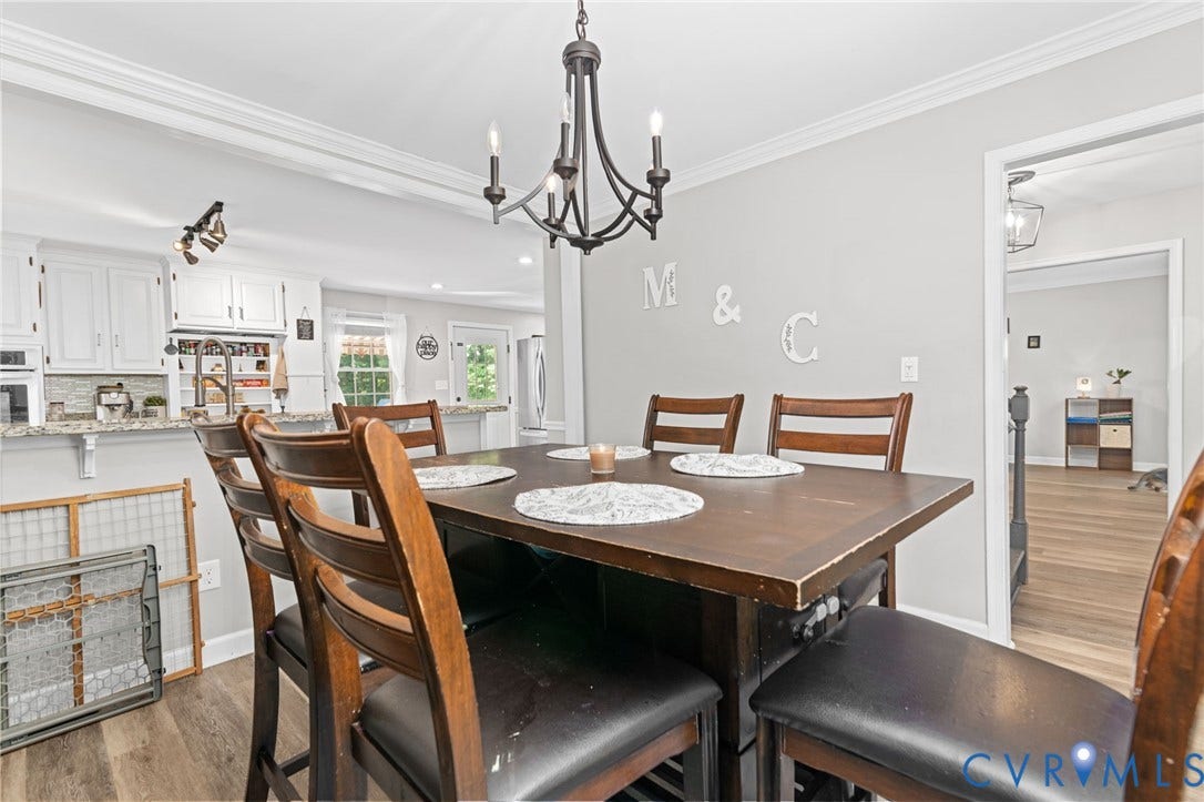 Crown molding details, wood-finish flooring, white cabinetry, granite-style countertops, and a black chandelier