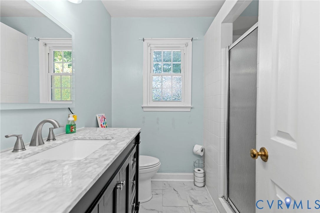 Vanity with a white countertop and undermount sink, brushed nickel faucet, tiled flooring, and a shower enclosure
