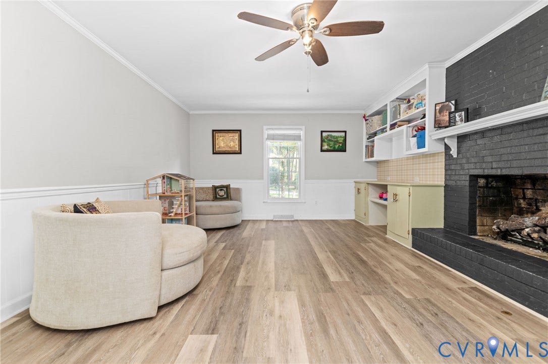 Wood-finish flooring throughout, white crown molding, built-in shelving, painted brick fireplace, and ceiling fan