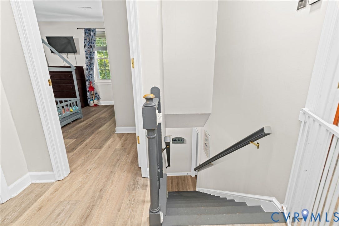 Wood-finish flooring throughout, white trim, and a gray painted staircase with a handrail