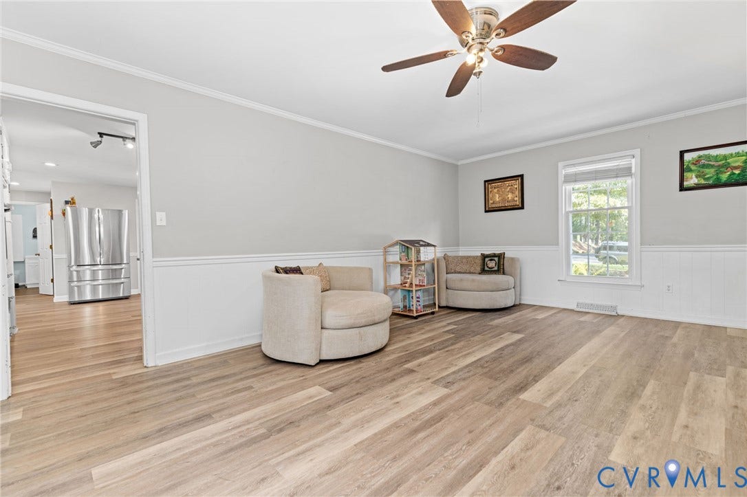 Spacious living area featuring wood-finish flooring, white wainscoting, and a ceiling fan