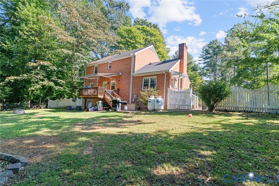 Brick exterior with a multi-level wood deck, a white privacy fence, and a brick chimney