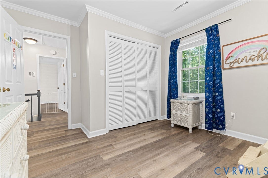 Wood-finish flooring, white louvered closet doors, bright window, and crown molding