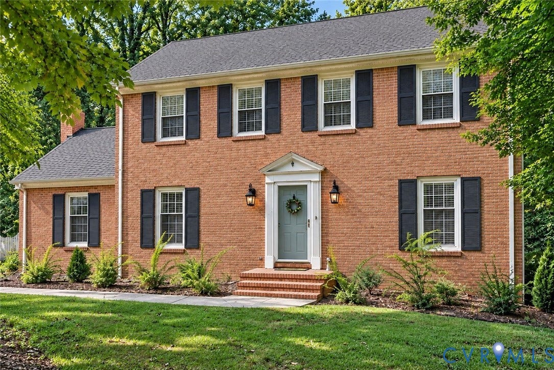 Brick exterior with contrasting dark shutters, a classic front entry with sidelights, and exterior lighting fixtures