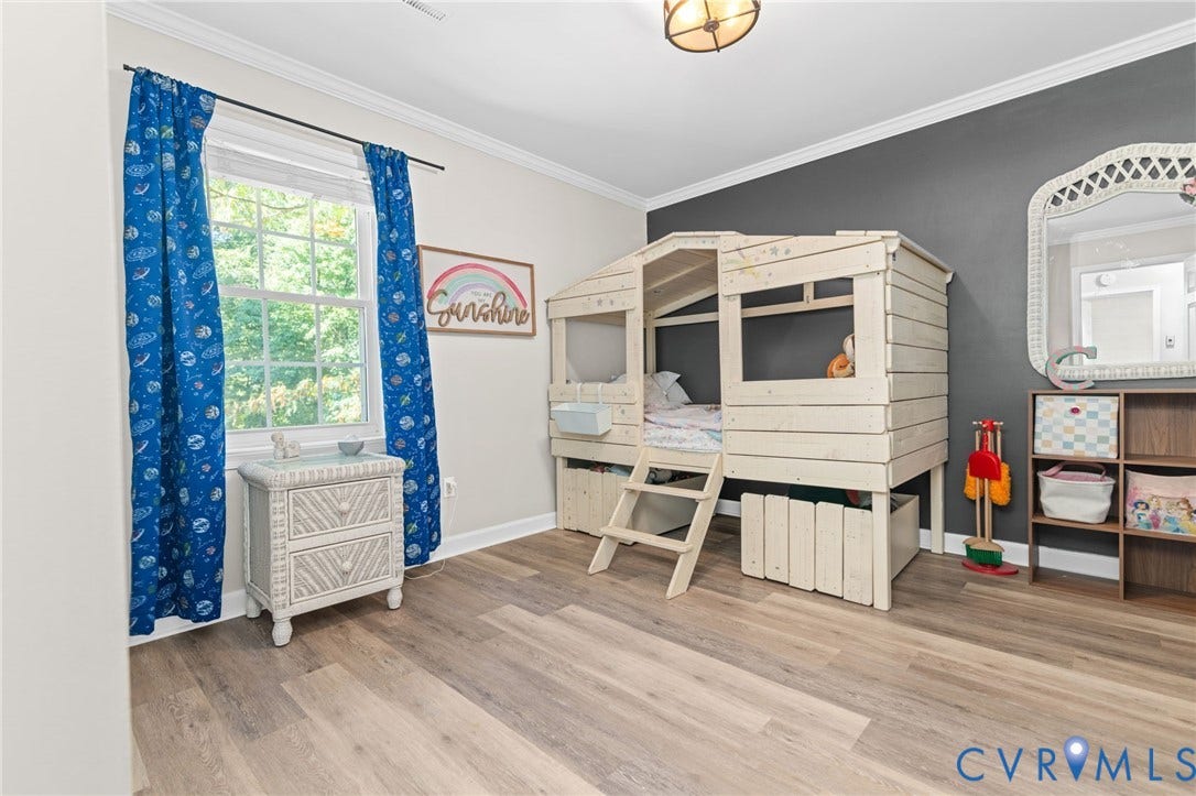 Wood-finish flooring throughout, single-pane window, crown molding, and a partial dark accent wall